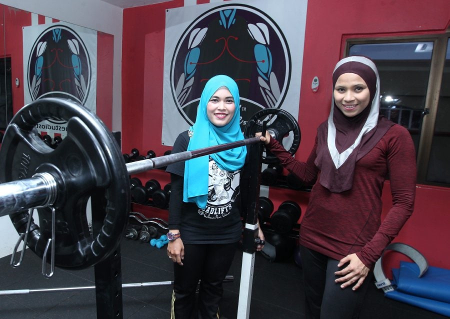 2 smiling girls next to barbell